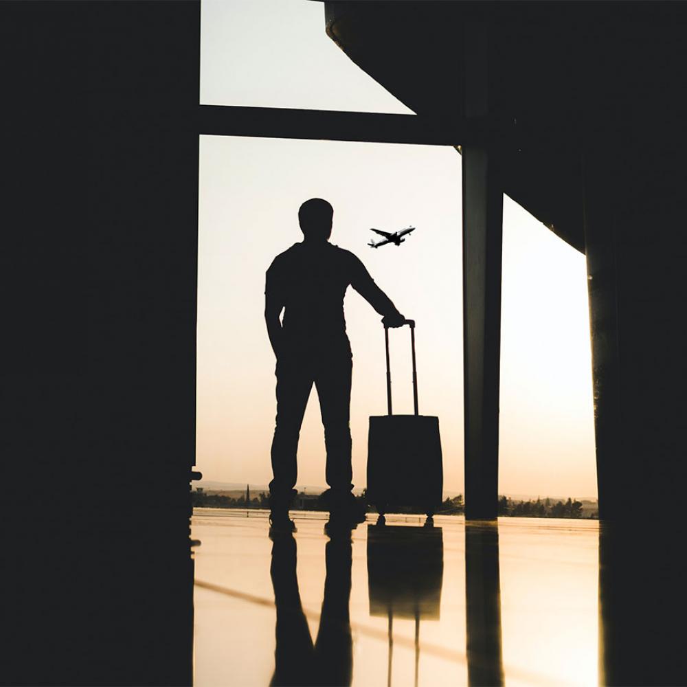 A man standing with his bags looking up at a plane