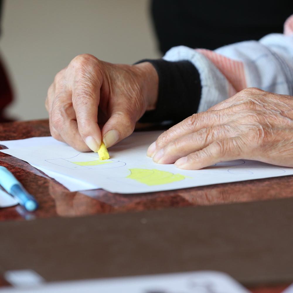 A senior citizen drawing with crayons